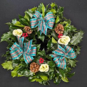 Holly graveside Christmas wreath with teal tartan bows, ivory rose accents, pinecones and red berries