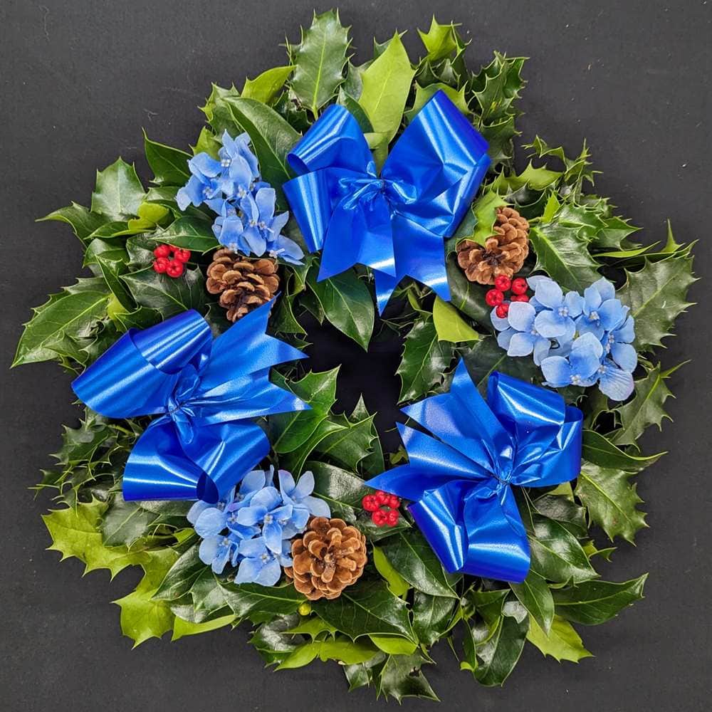 Holly graveside Christmas wreath with royal blue bows, blue floral accents, pinecones and red berries
