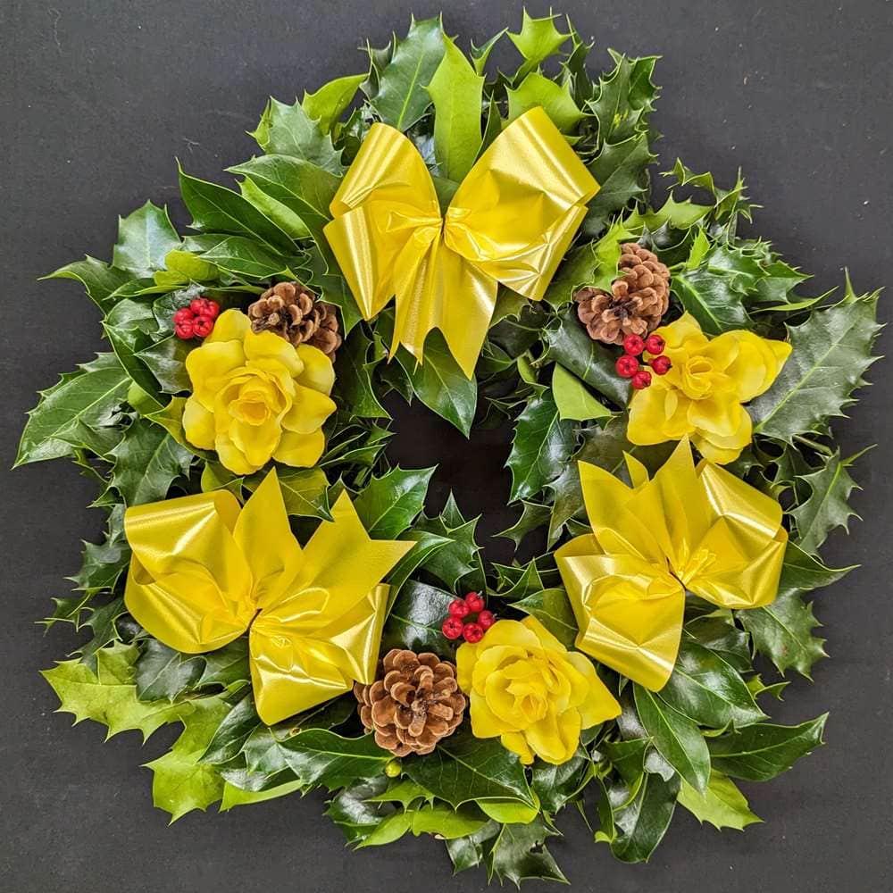 Holly graveside Christmas wreath with yellow bows, yellow rose accents, pinecones and red berries