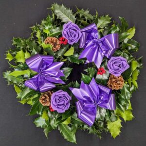 Holly graveside Christmas wreath with purple bows, purple rose accents, pinecones and red berries