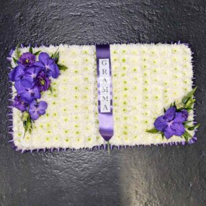 Open book funeral flower tribute with white chrysanthemums and purple orchids