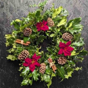 Traditional holly graveside wreath with red poinsettia accents, pinecones and cinnamon