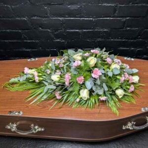 White rose and pink carnation single ended funeral spray with lisianthus and eucalyptus, displayed on a coffin