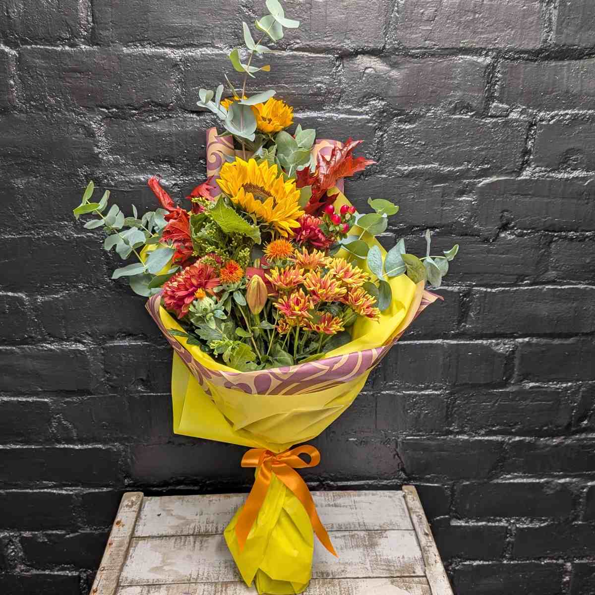 Autumn Glow hand-tied bouquet with sunflowers, orange chrysanthemums, berries and eucalyptus in bright yellow wrap with orange ribbon – Anastasia Florists Aberdeen