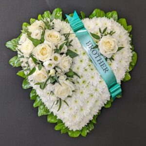 White chrysanthemum heart funeral tribute with white roses, green leaf collar and teal Brother ribbon on a dark background