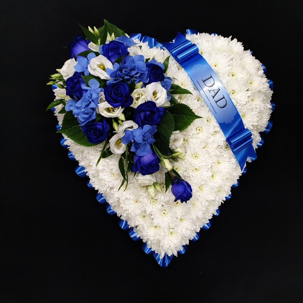 What Flower Arrangements are Suitable for a Male Funeral? White chrysanthemum heart funeral tribute with blue and white flowers and blue Dad ribbon on a black background