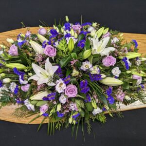 Lilac and blue coffin spray with white lilies on wooden coffin