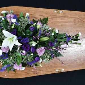 Lilac and purple lily single ended funeral spray on a wooden coffin with lisianthus and mixed greenery.