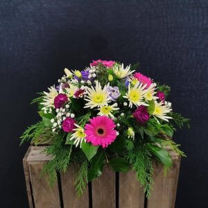 Miniature bright mixed funeral posy with pink gerbera, chrysanthemums and lilac flowers on a wooden crate