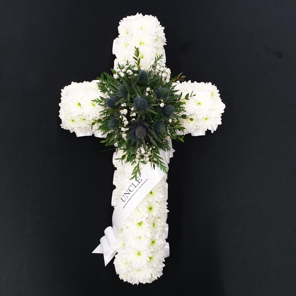 Funeral Flower Tributes Explained: Coffin Sprays, Wreaths, Hearts, Posies & More White flower cross funeral tribute with greenery
