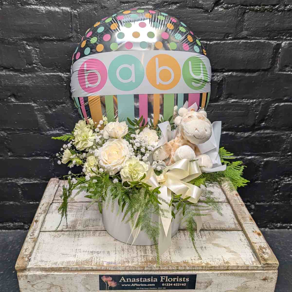 New baby gift with colourful “Baby” balloon, soft toy and cream and white flower arrangement in a white hat box on a wooden crate – Anastasia Florists Aberdeen