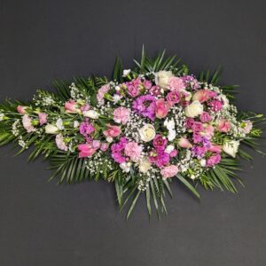 Pink and lilac single ended funeral spray with roses, carnations and gypsophila on a dark background.