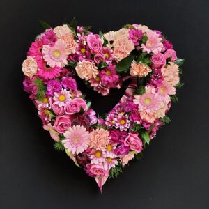 Pink open heart funeral tribute with roses, gerbera, carnations and chrysanthemums on a black background
