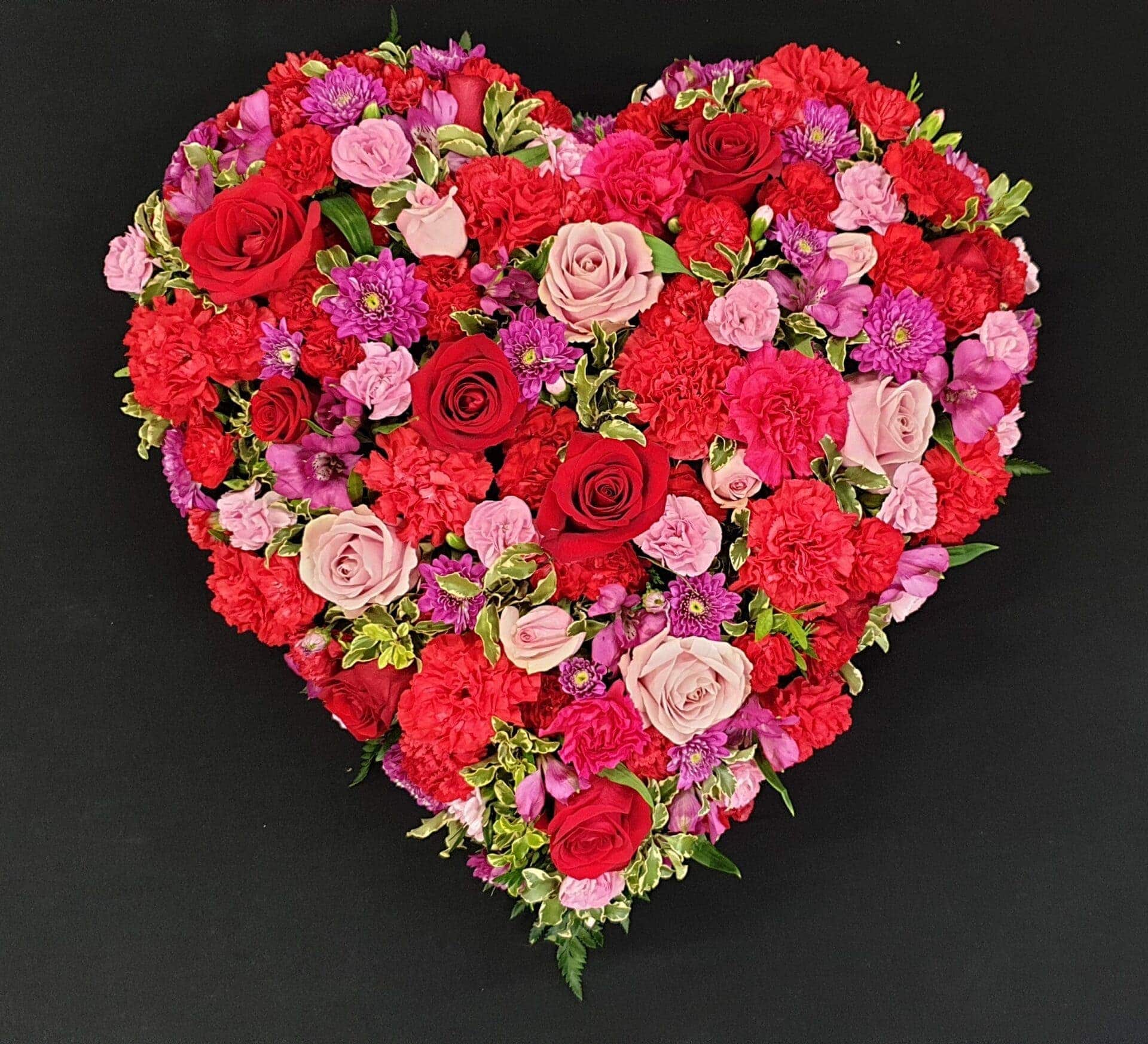 Red and pink luxury heart funeral tribute with roses and carnations on a black background