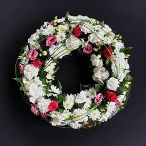 White funeral wreath with red roses, pink lisianthus and looping greenery