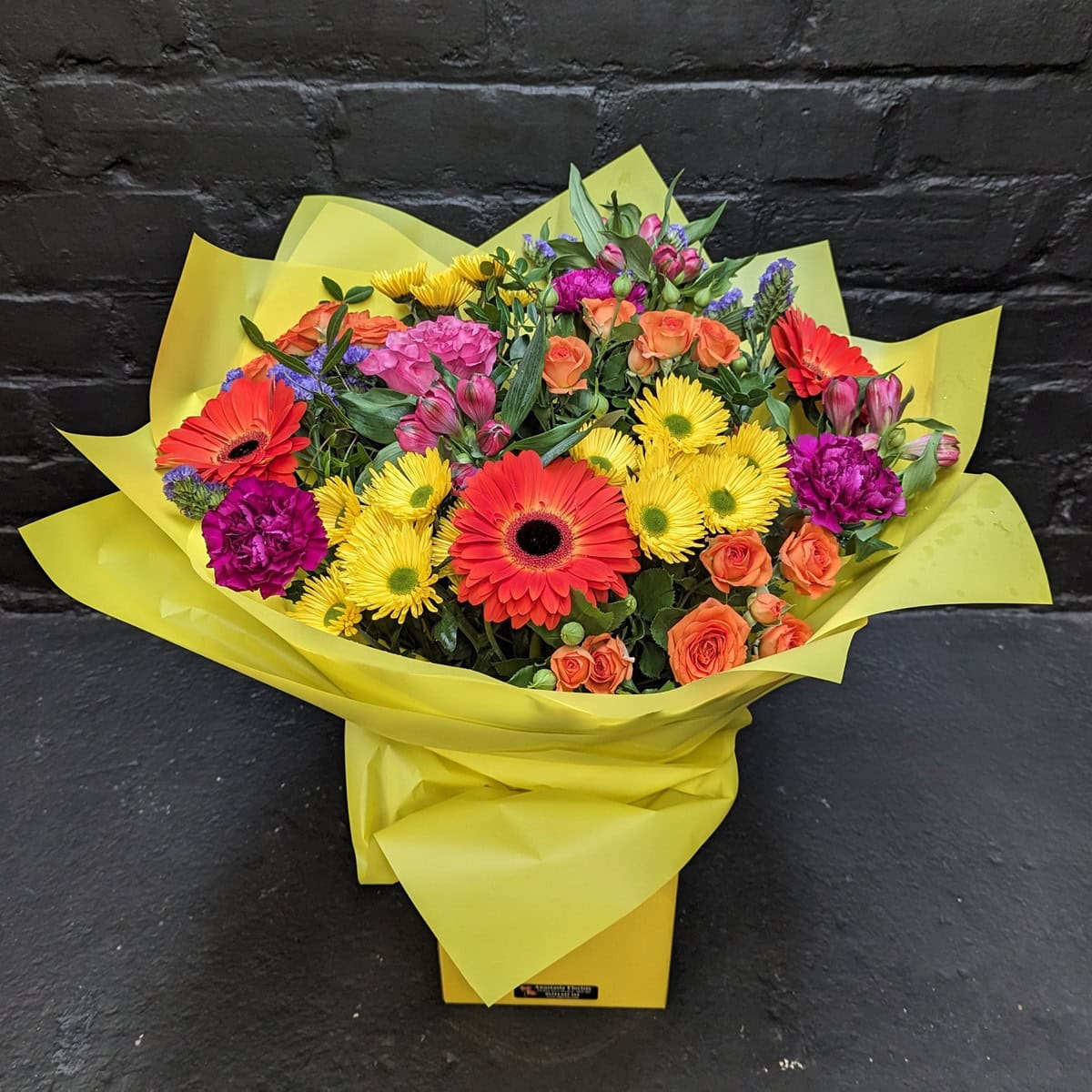 Sophia Bouquet bright mixed flowers with orange gerberas, yellow daisies, orange spray roses and pink blooms in a yellow gift box – Anastasia Florists Aberdeen
