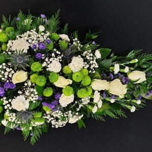 Thistle and lime green single ended funeral spray with ivory roses, white carnations and purple flowers on a black background.