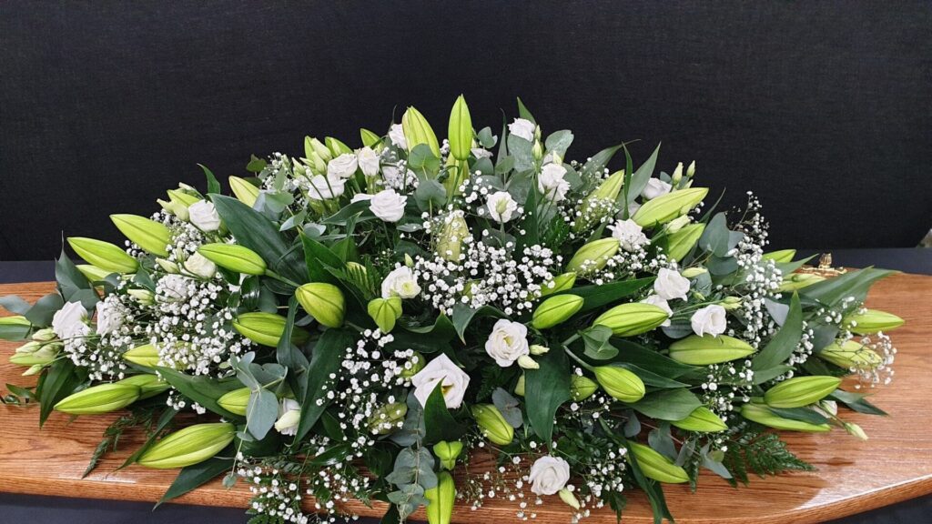 What Flower Arrangements are Suitable for a Male Funeral? White lily and rose coffin spray with gypsophila on wooden coffin