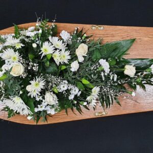 White rose and chrysanthemum single ended funeral spray on a wooden coffin with carnations and mixed greenery.