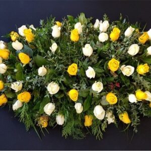 Yellow and white rose coffin spray with greenery on dark background