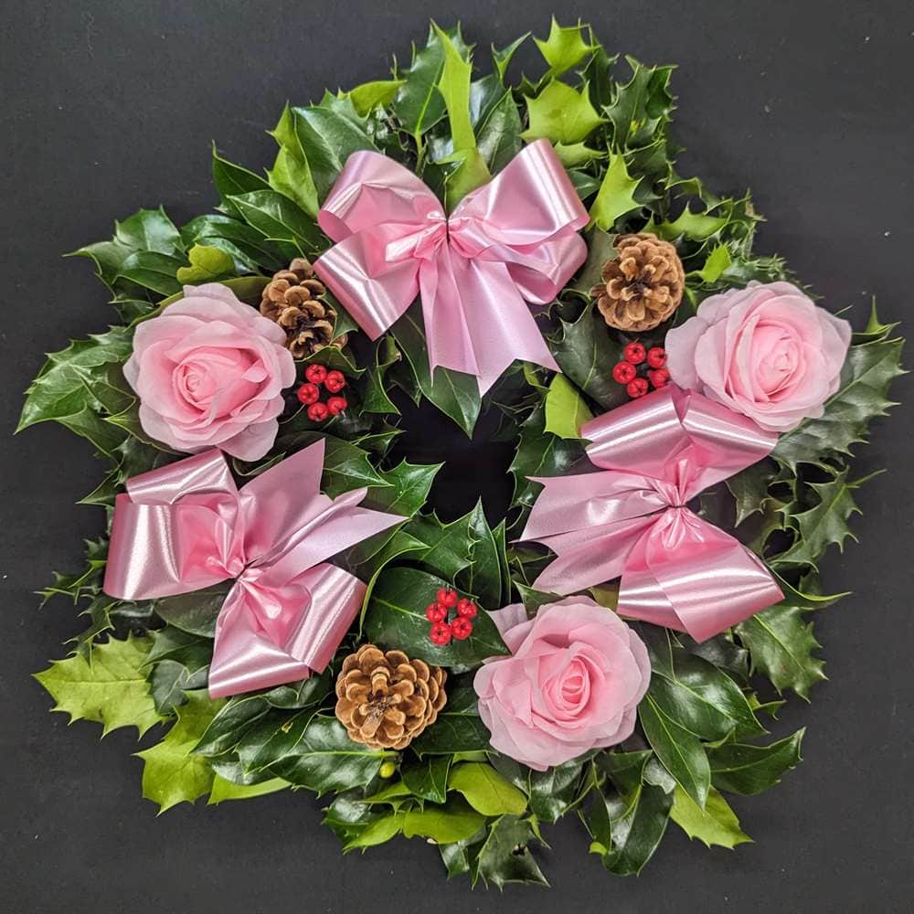 Holly wreath with pink roses, berries, and ribbons