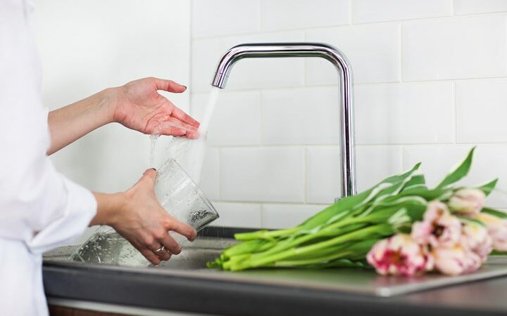 Young woman rinsing and cutting flowers and pouring water into the vase in kitchen sink. Close up