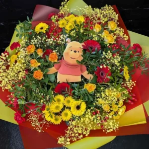 Anastasia Florists Top-down view of a colourful red and yellow bouquet with yellow roses, red and yellow gerberas, berries, greenery and a printed character topper.