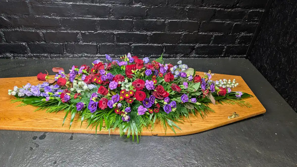 Colourful Mixed Flower Coffin Spray Wide view - Colourful mixed flower coffin spray with red and purple flowers on a wooden coffin