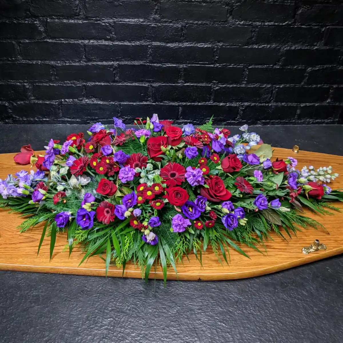 Colourful Mixed Flower Coffin Spray Colourful mixed flower coffin spray with red and purple flowers on a wooden coffin