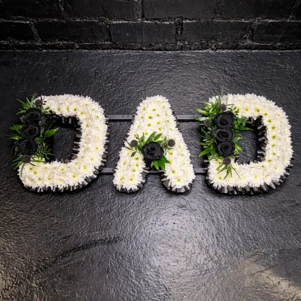 What Flower Arrangements are Suitable for a Male Funeral? Dad funeral letter tribute in black and white flowers arranged on a frame