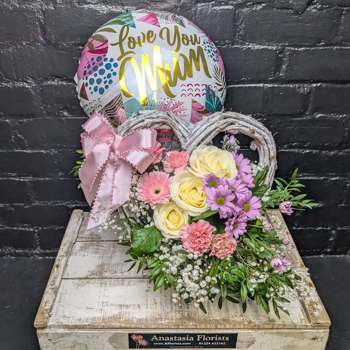 I Love You Mum Flower Basket Side View - Heart-shaped wicker basket with pink roses, purple daisies, and a Love You Mum balloon for Mother's Day.