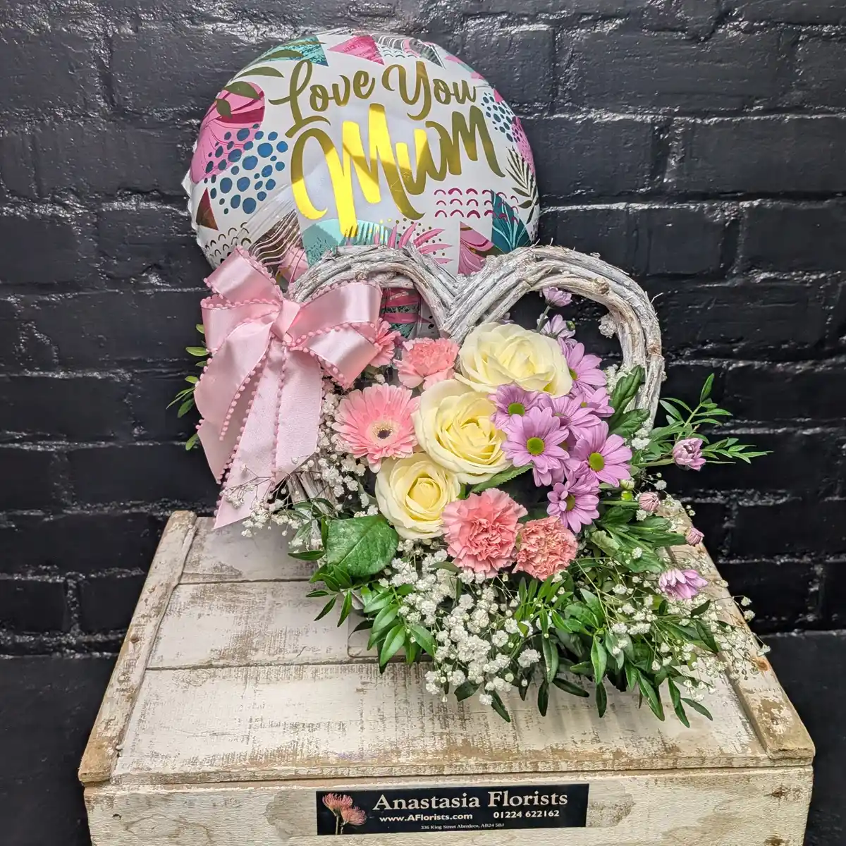 I Love You Mum Flower Basket Heart-shaped wicker basket with pink roses, purple daisies, and a Love You Mum balloon for Mother's Day.