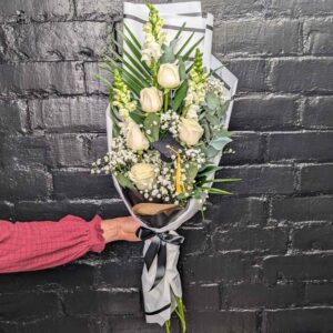 A florist in aberdeen holding a tall white rose and antirrhinum graduation presentation bouquet with a miniature graduation cap against a black brick wall.