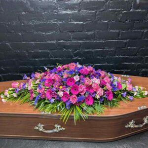Double-ended funeral coffin spray featuring vibrant cerise gerberas, pink roses, and deep purple flowers, hand-crafted by Anastasia Florists in Aberdeen.
