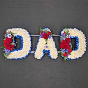 DAD funeral floral letters in blue and white team colours, massed with white chrysanthemums with red roses, thistle and purple flowers