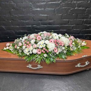 Pink and white double-ended casket spray with white hydrangea, pink roses, gerbera and gypsophila, resting on a wooden coffin