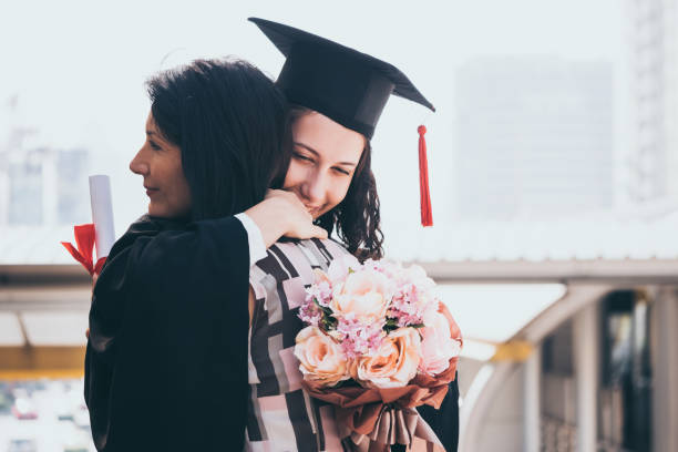 A daughter holds flowers while hugging her mother at her graduation