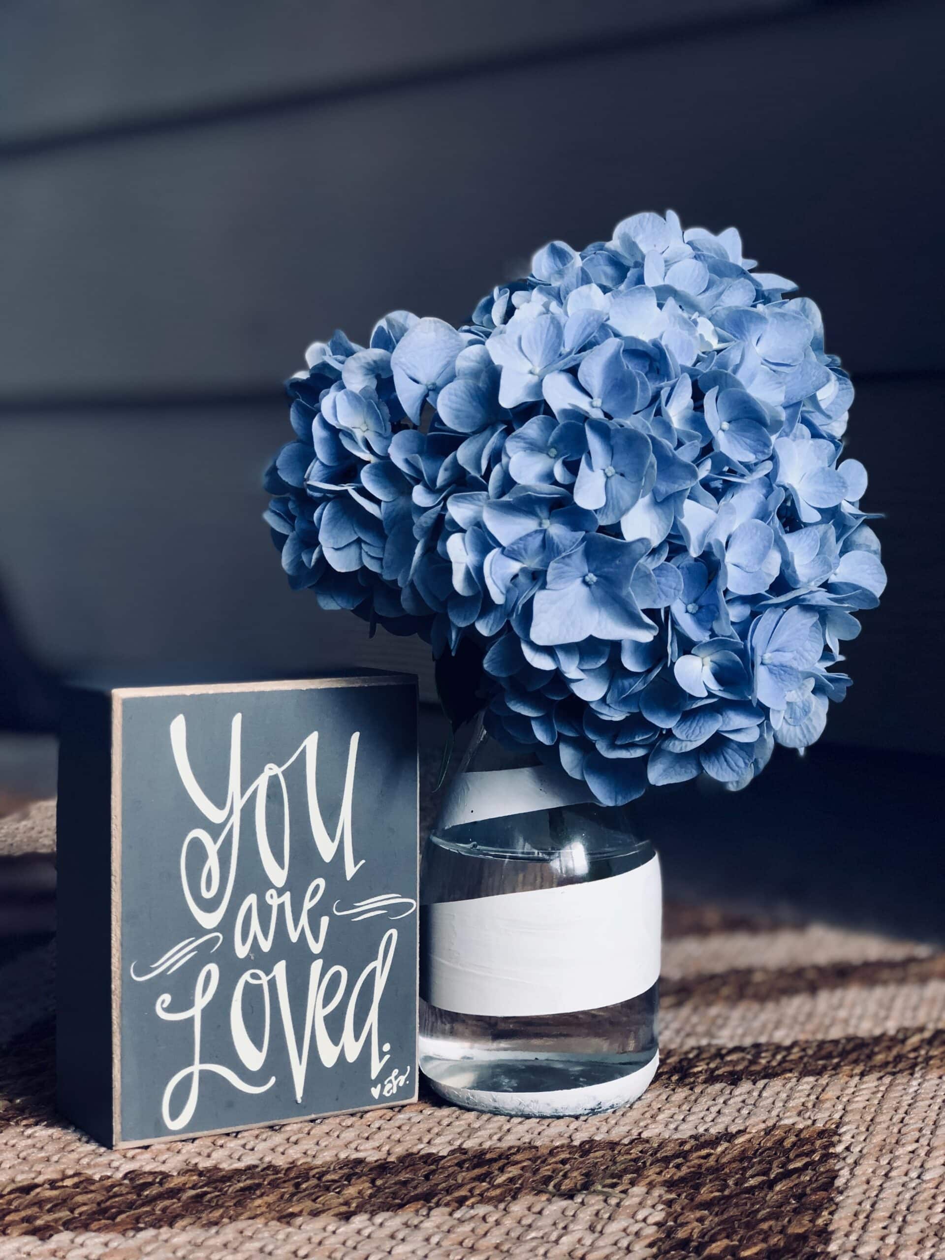 Blue hydrangea in a bottle vase with a text "You are Loved"