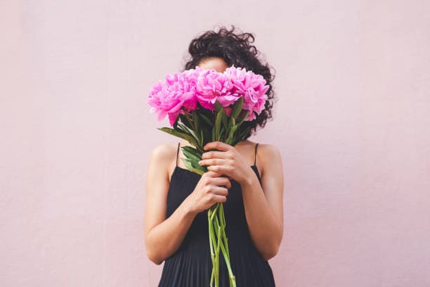 selecting blooms for a flower bouquet Woman holding a bouquet of pink flowers and concealing her face